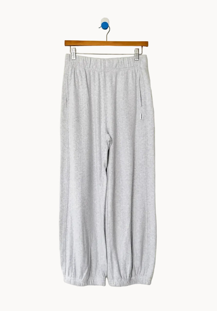 Pale grey cotton sweatpants with elasticated cuffs hang on a wooden clip hanger against an off-white background