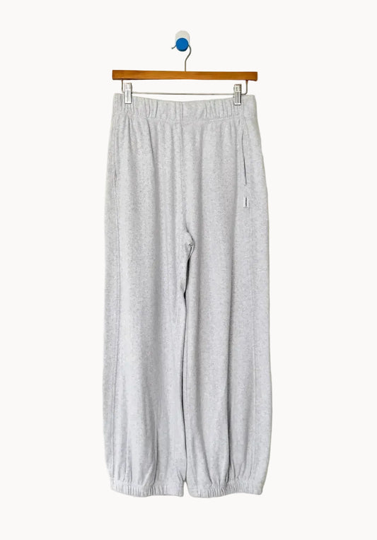 Pale grey cotton sweatpants with elasticated cuffs hang on a wooden clip hanger against an off-white background