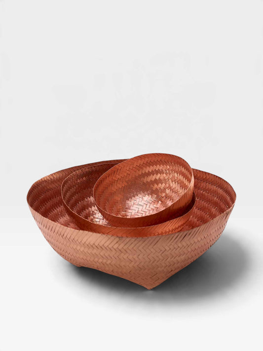 Three nested woven bowls in a warm copper tone, photographed on a clean light gray studio background.