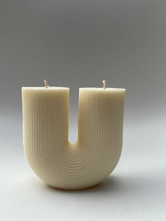 The front view of a u-shaped wax candle with ribbed detailing sits on a white surface against a soft gray background