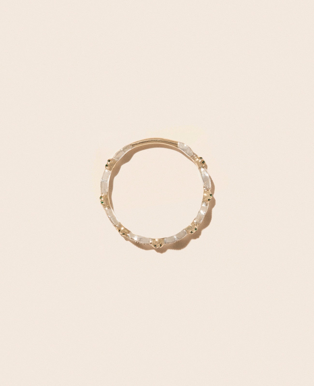 Gold, diamond, and emerald thin ring with shown laying flat on an off-white background