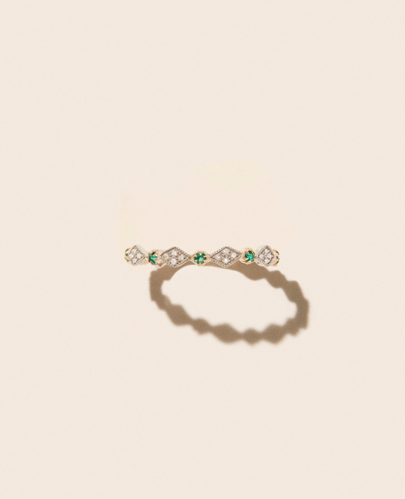 Gold, diamond, and emerald thin ring with diamond-shaped motif shown from front view against an off-white background