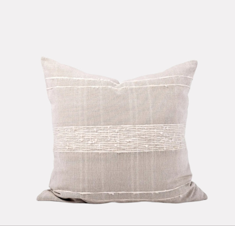 Square sand-colored wool and cotton pillow with woven ivory striping details sits against white background