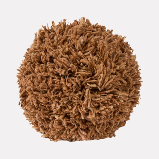 Light brown-colored spherical pillow made of tufted wool and sitting against a white backdrop