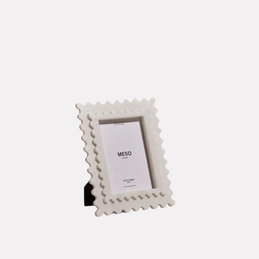 A white marble picture frame with scalloped edging set against a white backdrop