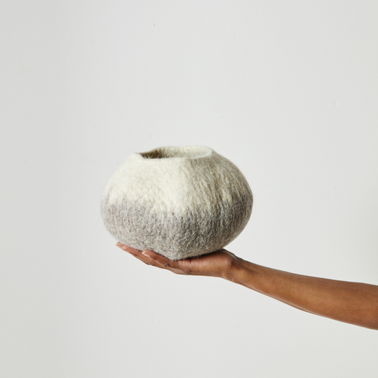 Woman's hand holding an ivory and grey ombre wool decorative basket against a white background