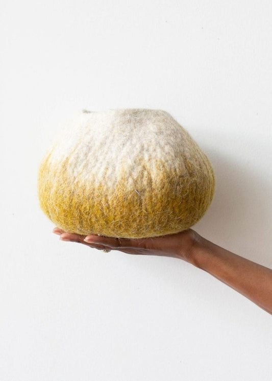 Woman's hand holding white and deep yellow ombre wool decorative basket against a white background