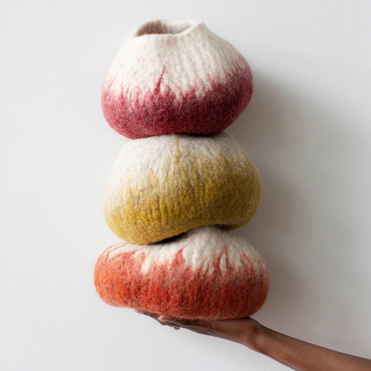 Woman's hand holding a stack of colorful ombre wool decorative baskets against a white background