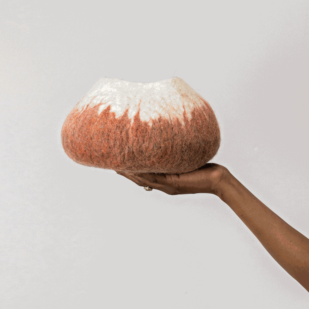 Woman's hand holding white and deep orange ombre wool decorative basket against a white background