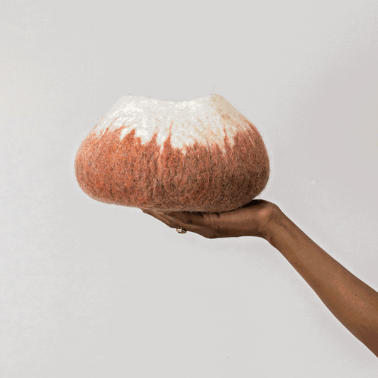 Woman's hand holding white and deep orange ombre wool decorative basket against a white background