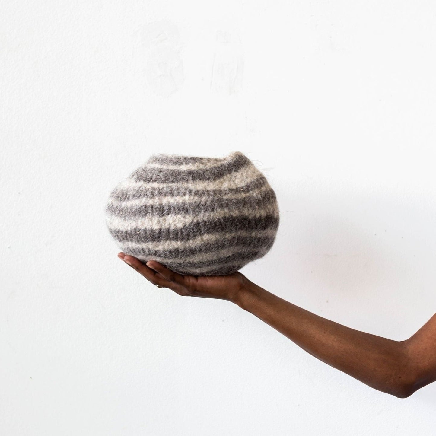 Woman's hand holding white and grey striped wool decorative basket against a white background