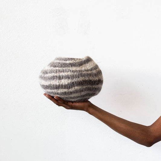 Woman's hand holding white and grey striped wool decorative basket against a white background