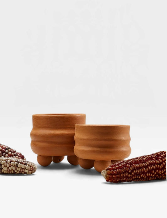 Two small terracotta pots with ribbed bodies and rounded feet, styled with dried corn cobs on a clean white background.