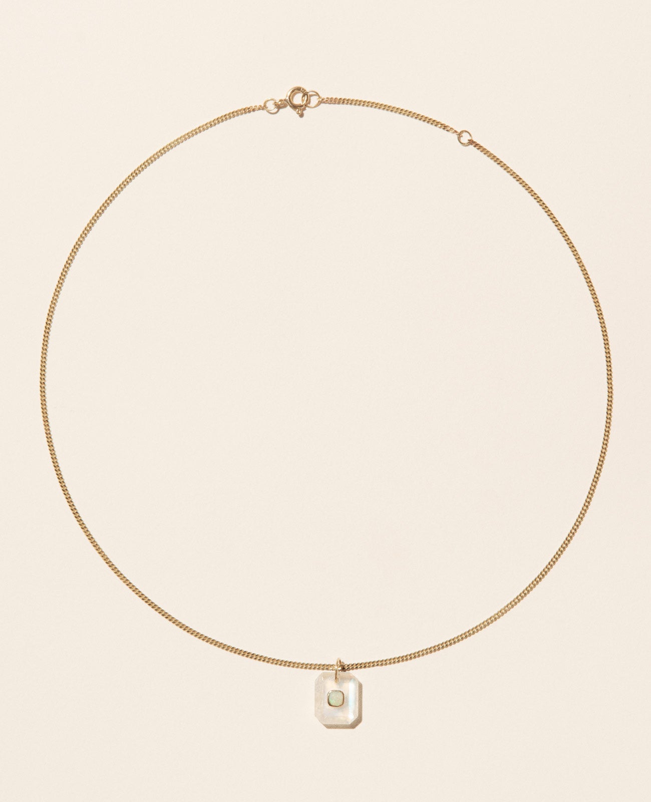 A gold chain necklace with a milky moonstone pendant featuring an opal in the center set in yellow gold and sitting on an off-white background