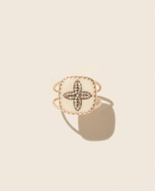 Rose gold double band ring featuring a square white resin medallion with a four petal diamond inlay sitting upright against an off-white background