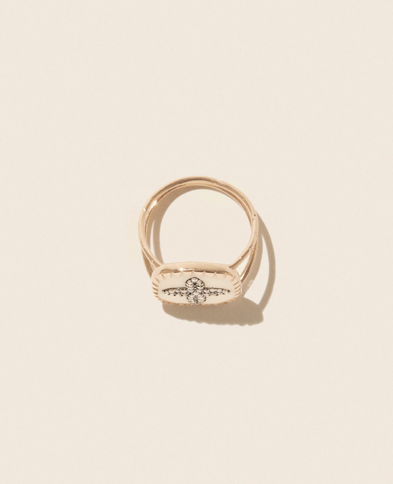 Rose gold double band ring featuring a square white resin medallion with a four petal diamond inlay laying on its side against an off-white background