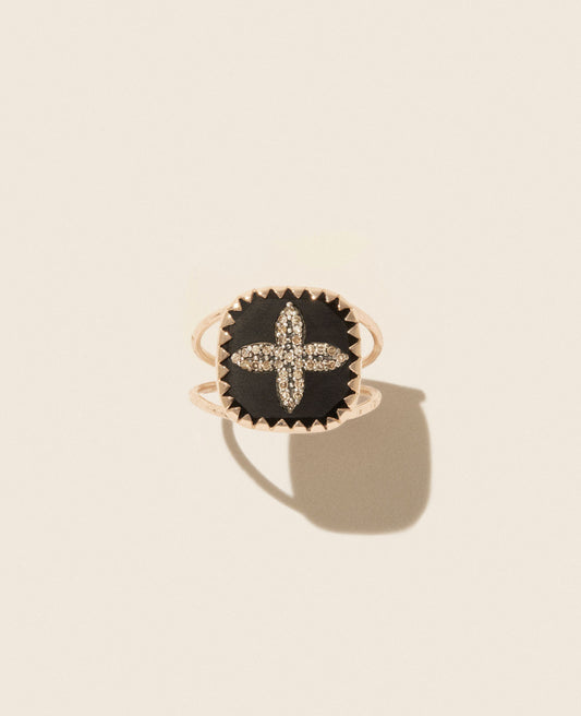 Double-banded rose gold ring facing upwards with square black resin medallion featuring four-petal shape diamond inlay set on an off-white background