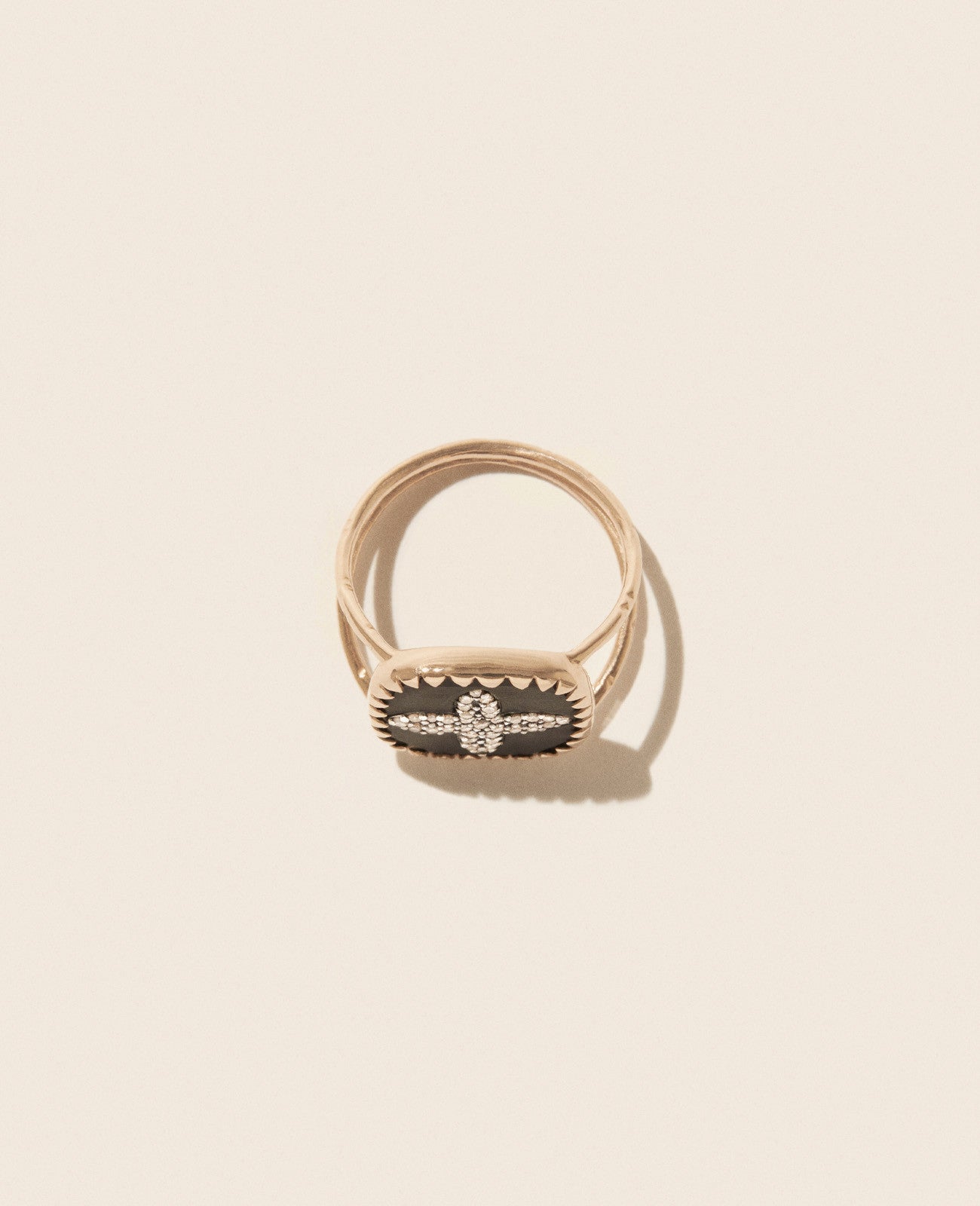 Double-banded rose gold ring with square black resin medallion featuring four-petal shape diamond inlay laying flat and set on an off-white background