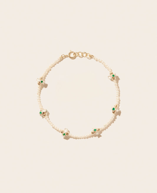 A stringed freshwater pearl bracelet with six clusters of gold beads, diamonds, and emeralds spaced evenly throughout and a gold clasp shown laid flat on an off-white background