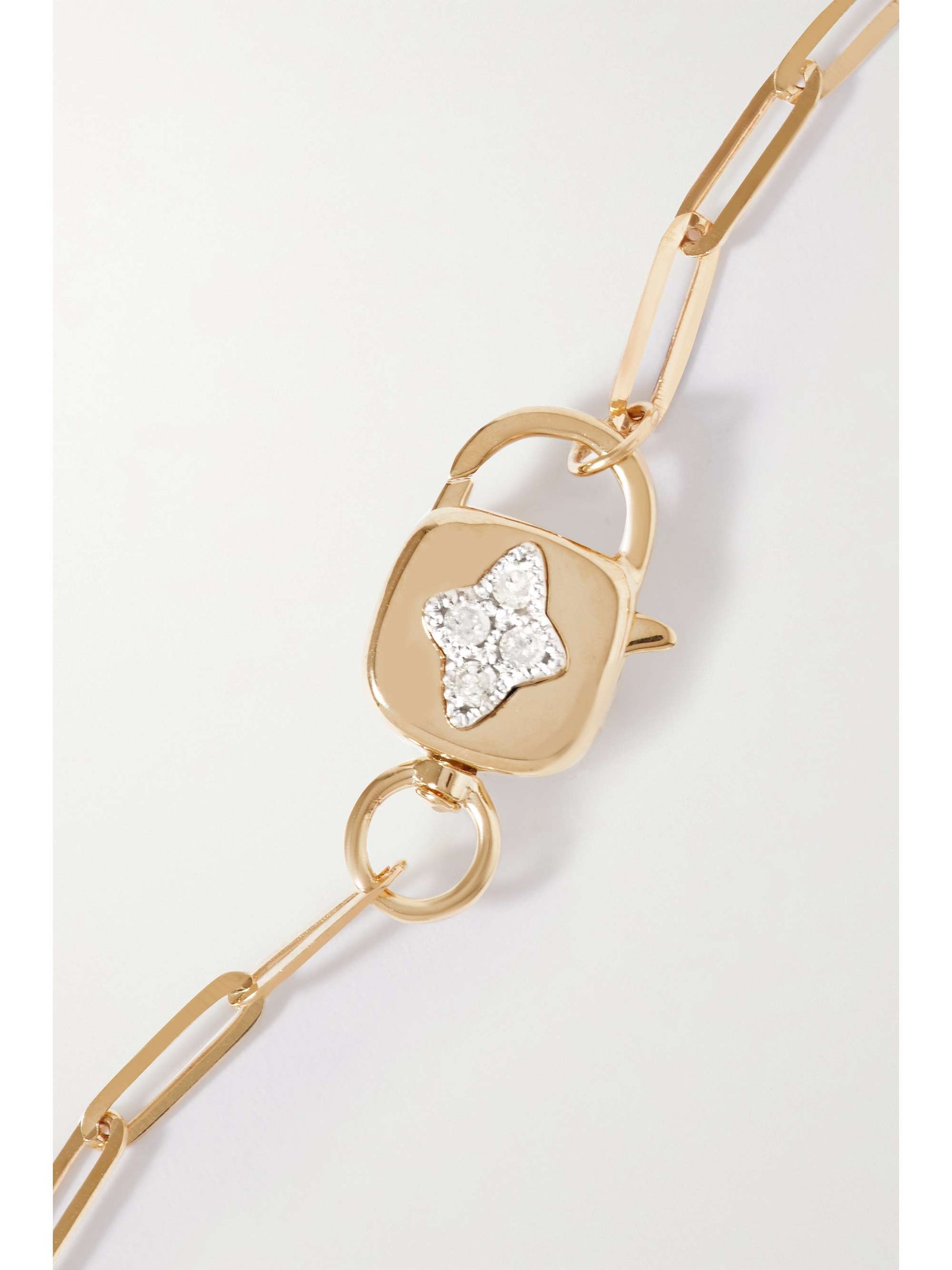 A closeup of a lock-shaped clasp featuring a diamond four-point star on a gold chainlink-style bracelet laying flat on a white background