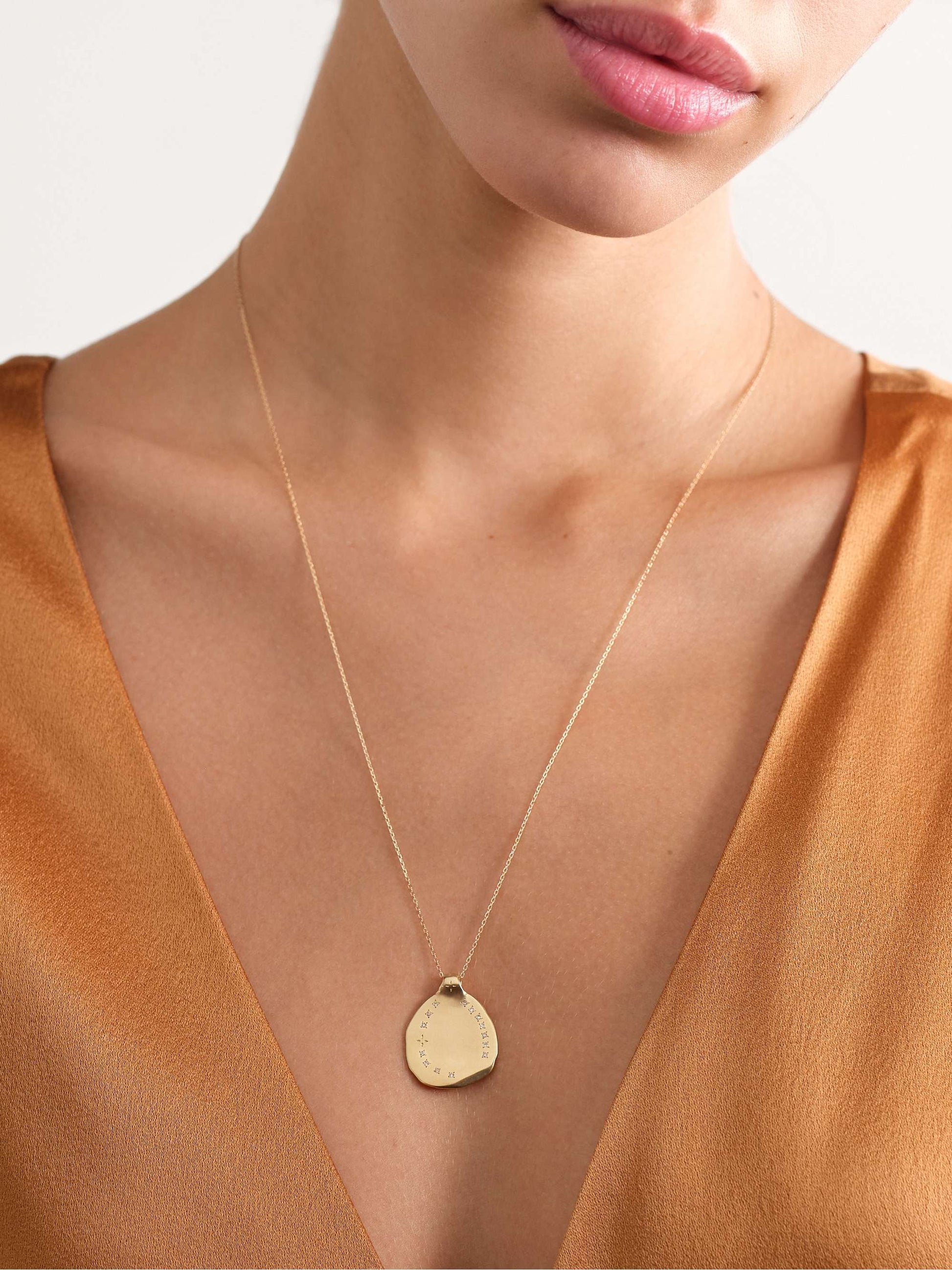 A view of the neck and chest of a woman in a bronze-colored v-neck blouse wearing a yellow gold necklace with an irregular shaped gold round pendant with ring of inlaid diamonds 