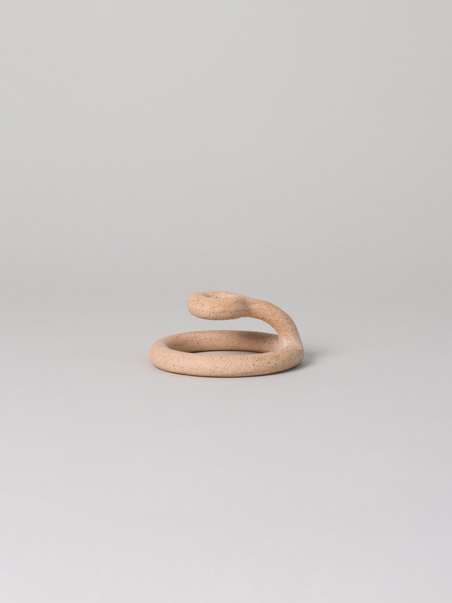 Sand-toned speckled clay candle holder in a coiled shape sits against a pale grey background