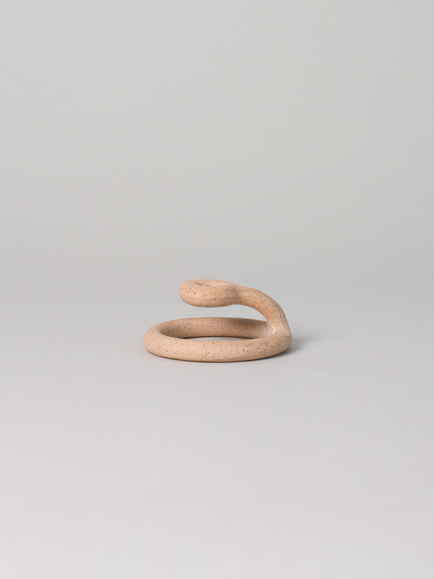 Sand-toned speckled clay candle holder in a coiled shape sits against a pale grey background