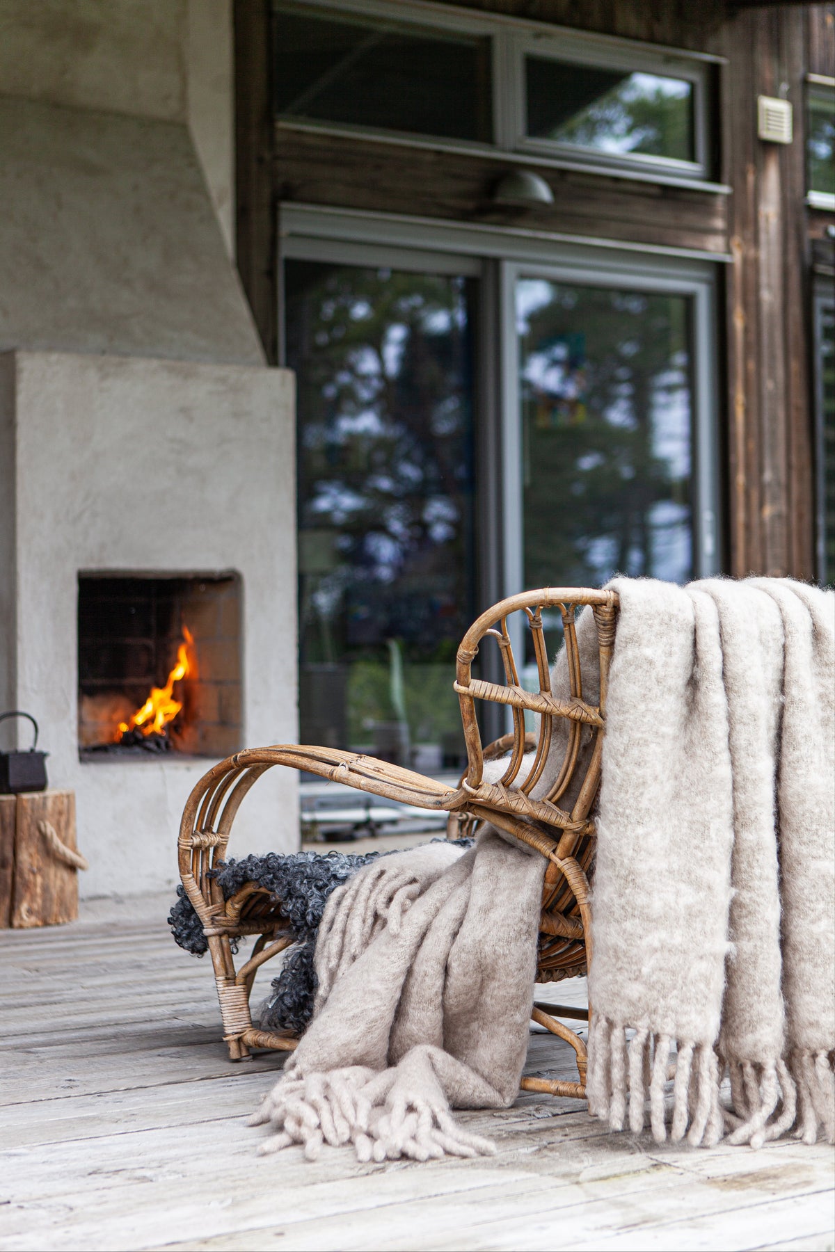 A luxury kid mohair blanket in light taupe color is draped over a wooden rack with a fire burning in the background, creating a cozy and elegant outdoor atmosphere.
