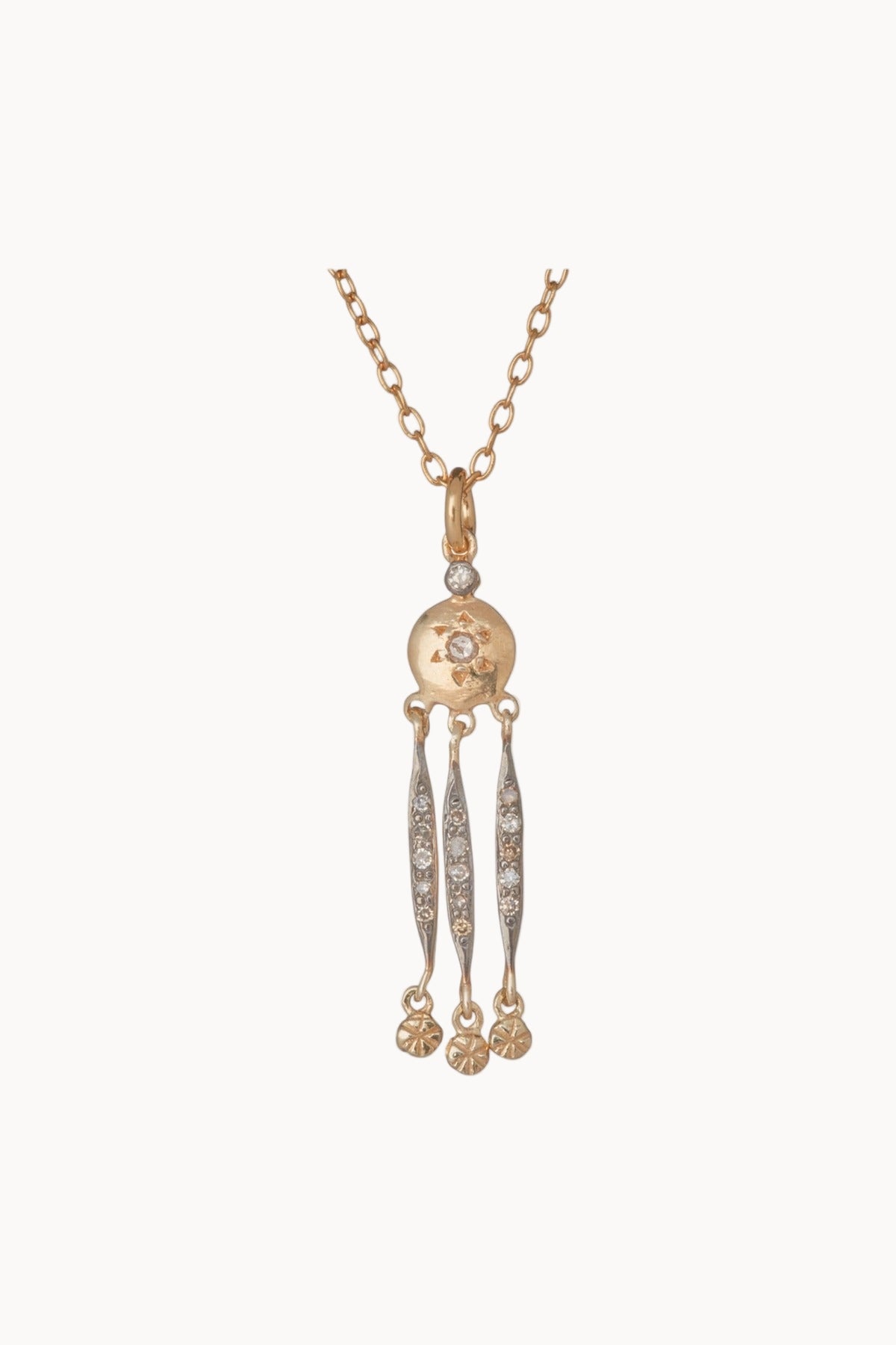 Gold chainlink necklace featuring a round gold and diamond pendant with delicate hanging elements hanging against a soft white background