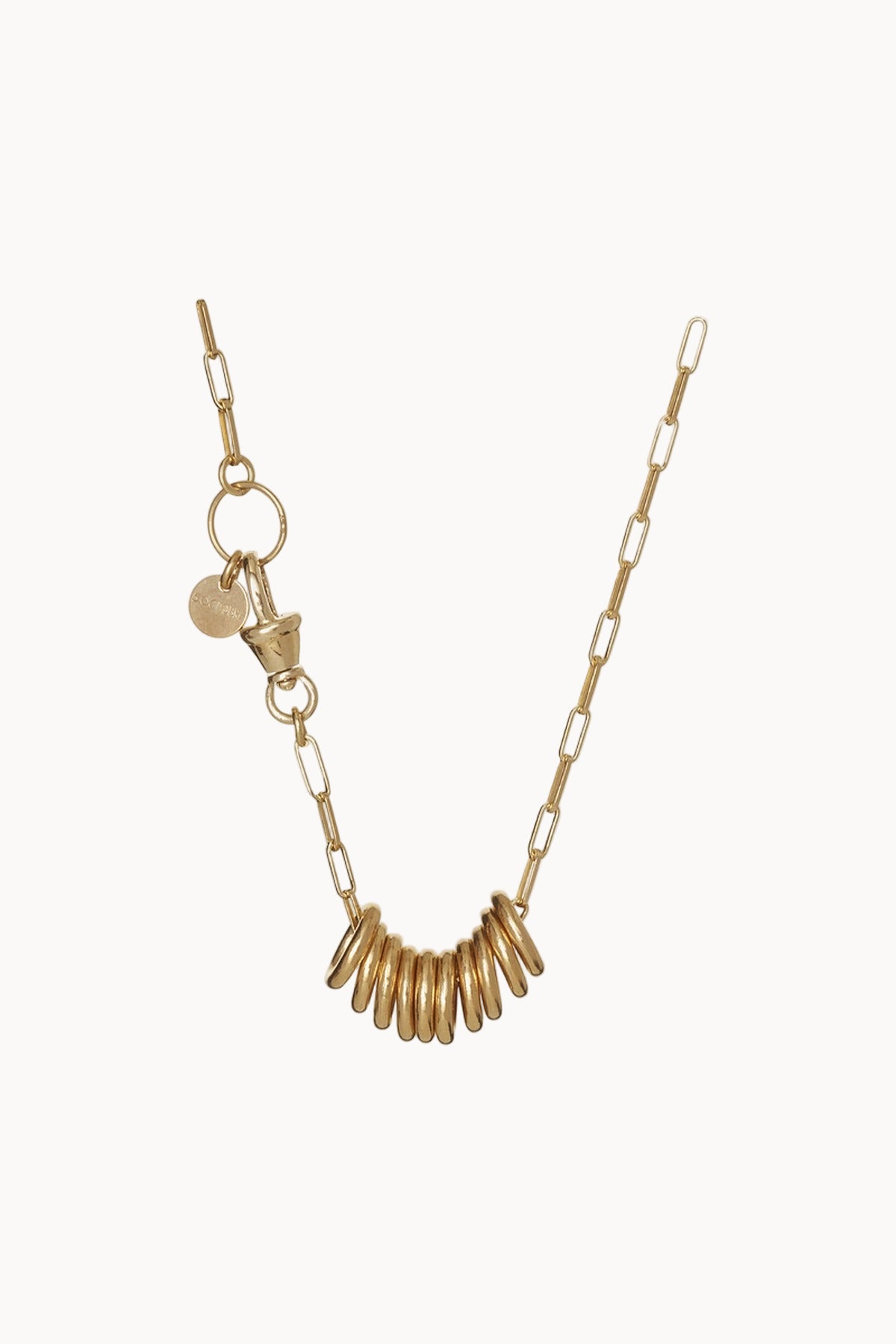 Gold chainlink necklace with golden rings and charms hanging against a soft white background