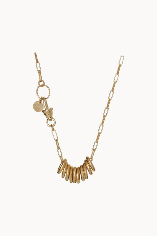Gold chainlink necklace with golden rings and charms hanging against a soft white background