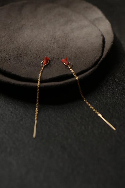 Gold threader earrings with red coral accent laying on a dark gray suede surface
