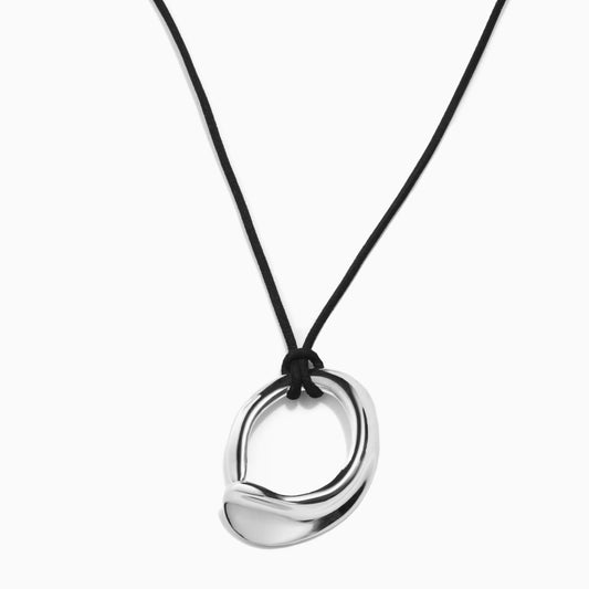 Silver pendant in an abstract circular shape hangs on a black cord against a white background
