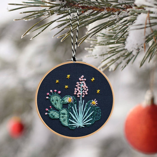 Embroidered ornament with cacti and flowers hanging on a Christmas tree.