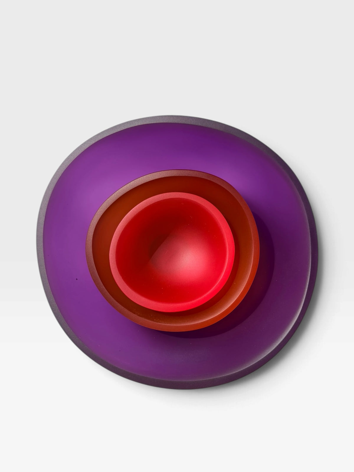 Three nesting bowls made of translucent resin in purple (large), orange (medium) and pink (small) set against a light gray background.
