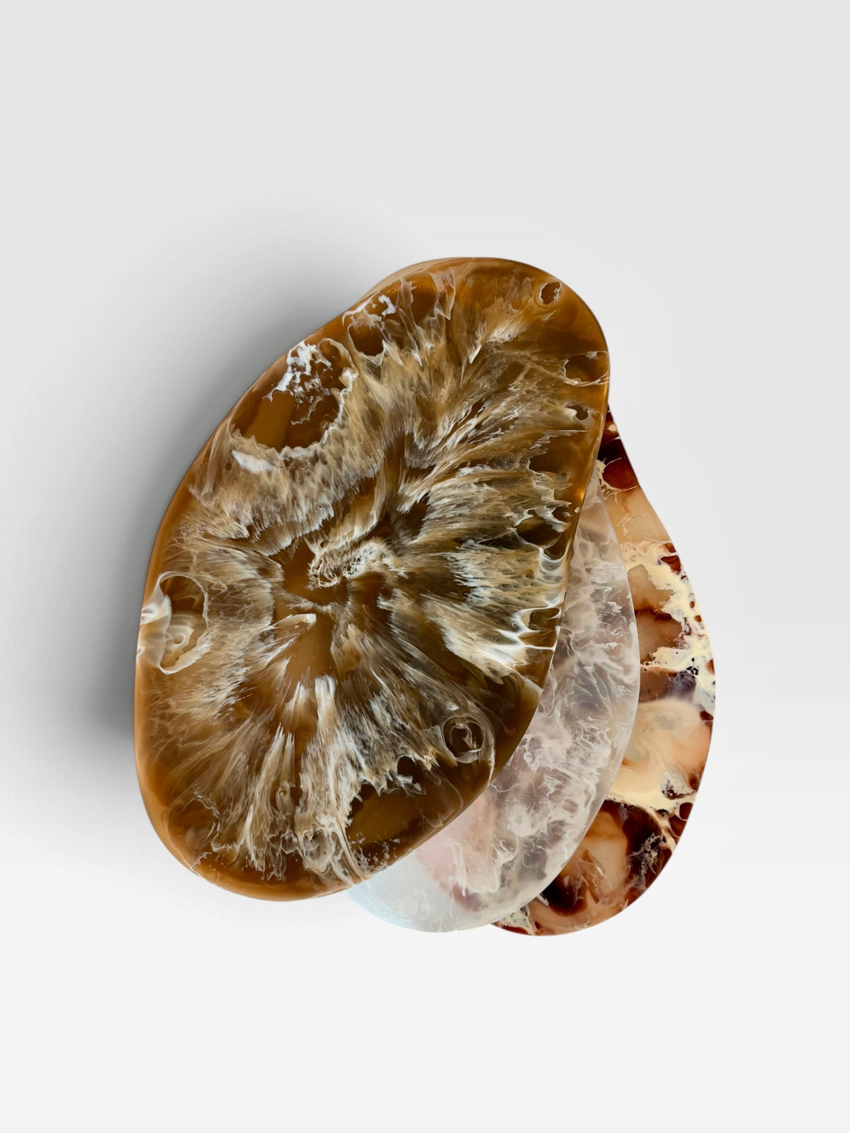 Three organic-shaped marbled resin platters with marbled brown, beige, and white patterns, stacked slightly offset on a light gray background.
