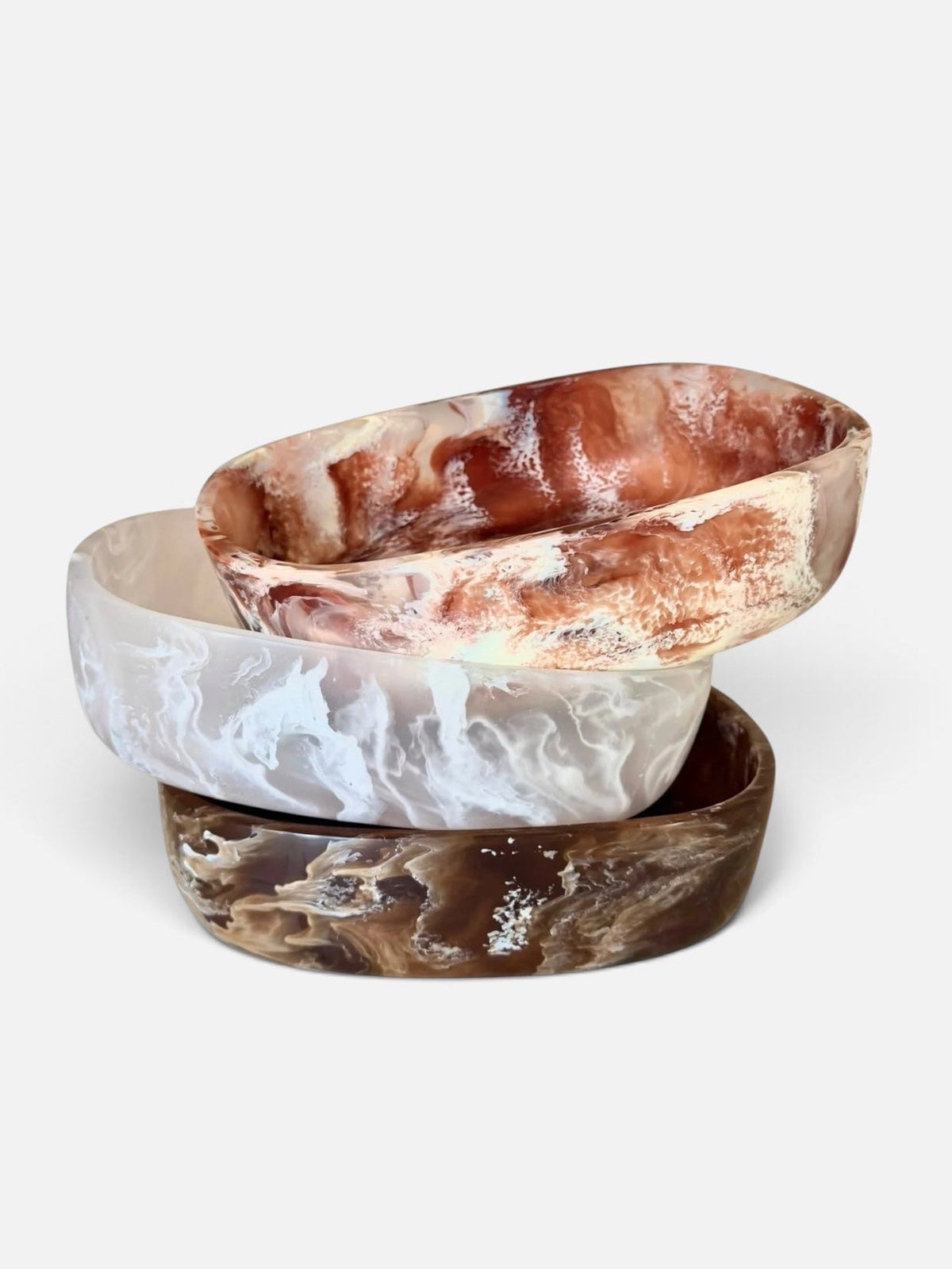 Three stacked oval bowls made of natural stone with marbled patterns in brown, white, and reddish tones, photographed on a clean light gray background.