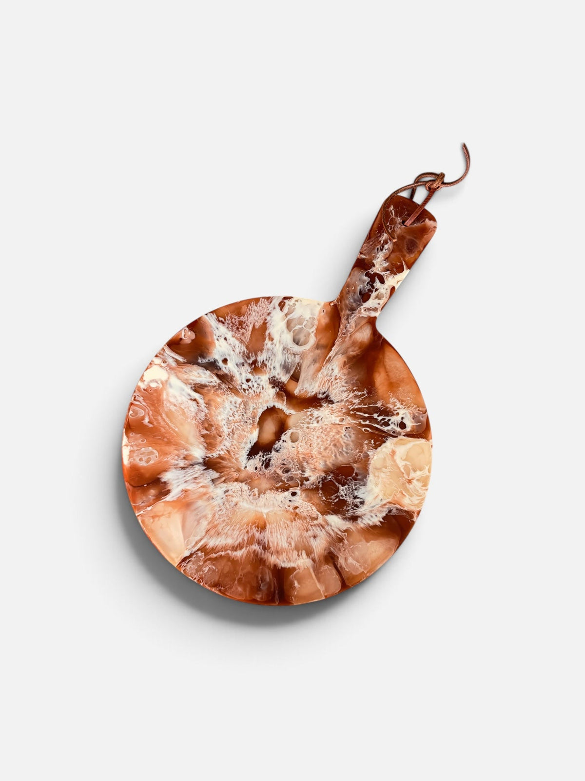 A round resin serving board in a brick red, white, and off-white marbled swirl pattern with a handle and leather hanging tie 