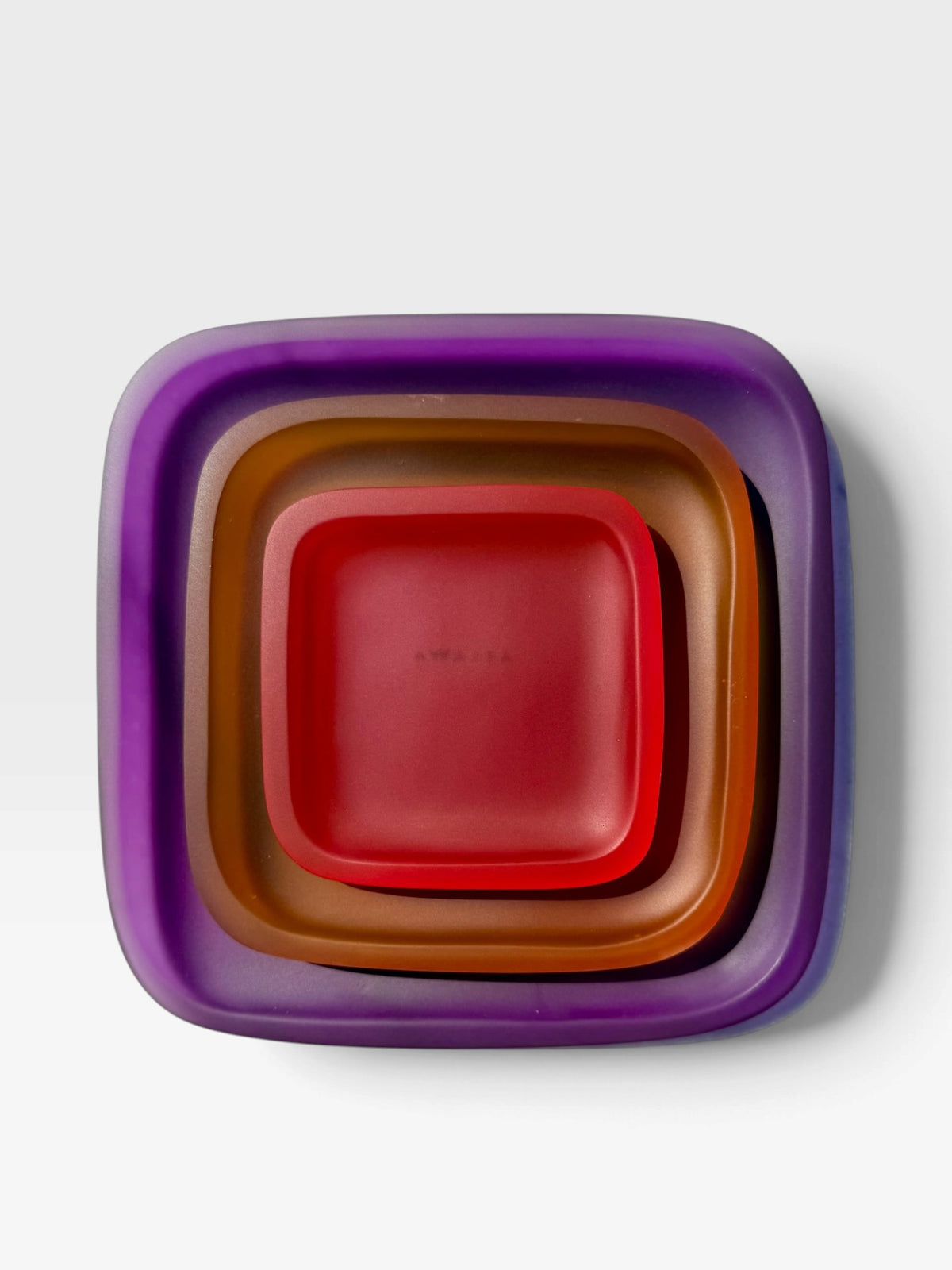 A set of nested square plates with rounded corners in purple, brown, and red, stacked concentrically on a light gray background.