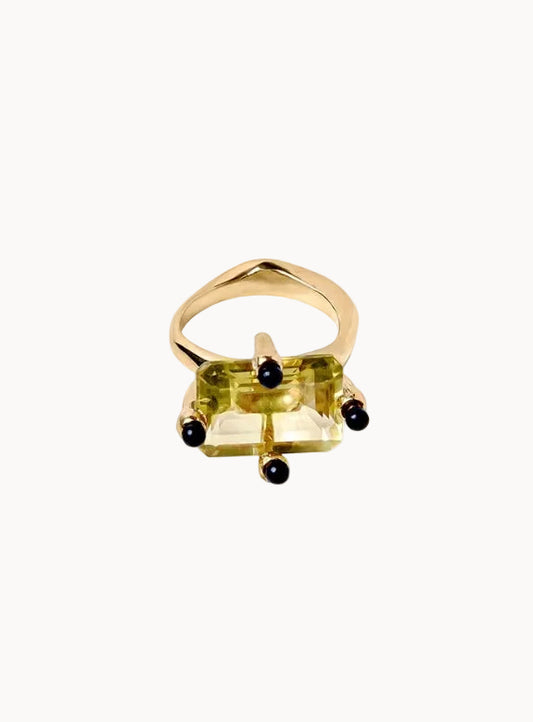 Gold ring with a yellow gemstone and black accents on a white background