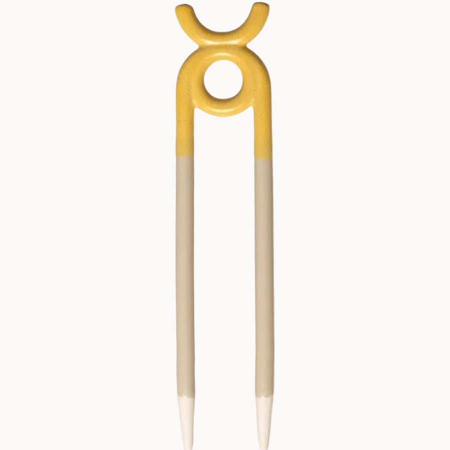 A ceramic garden stake with a yellow top featuring a circular cutout and a stylized crescent moon design, with two light beige sticks extending downward to pointed tips, shown on a solid cream background.