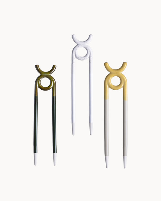 Three decorative ceramic plant stakes with a circular top loop and straight lower prongs, shown on a plain light background. The left pick is dark green and gold, the center pick is white, and the right pick is gold and silver.