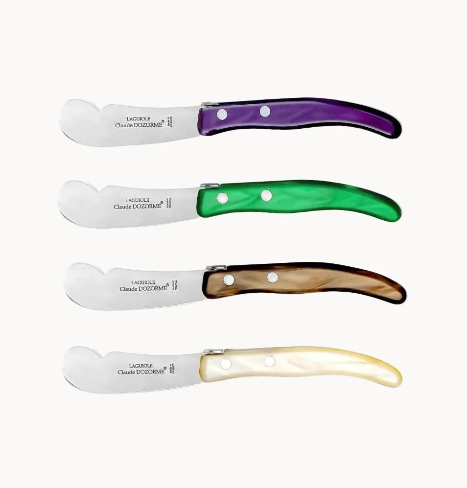 Four cheese knives with curved stainless steel blades and handles in purple, green, brown, and cream, arranged vertically on a light gray background.
