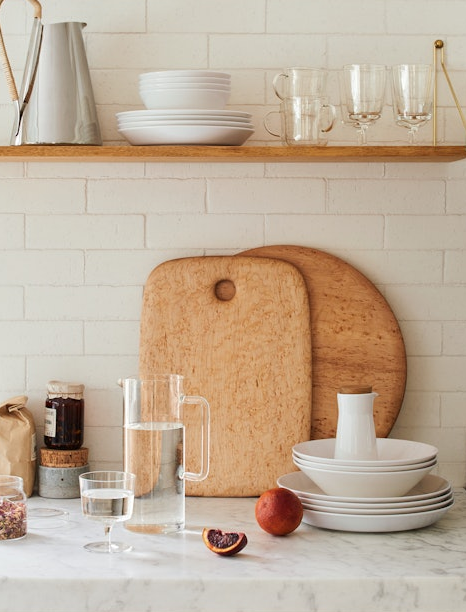 Kitchen counter with white dishes, glasses, and wooden cutting boards against a tiled wall.