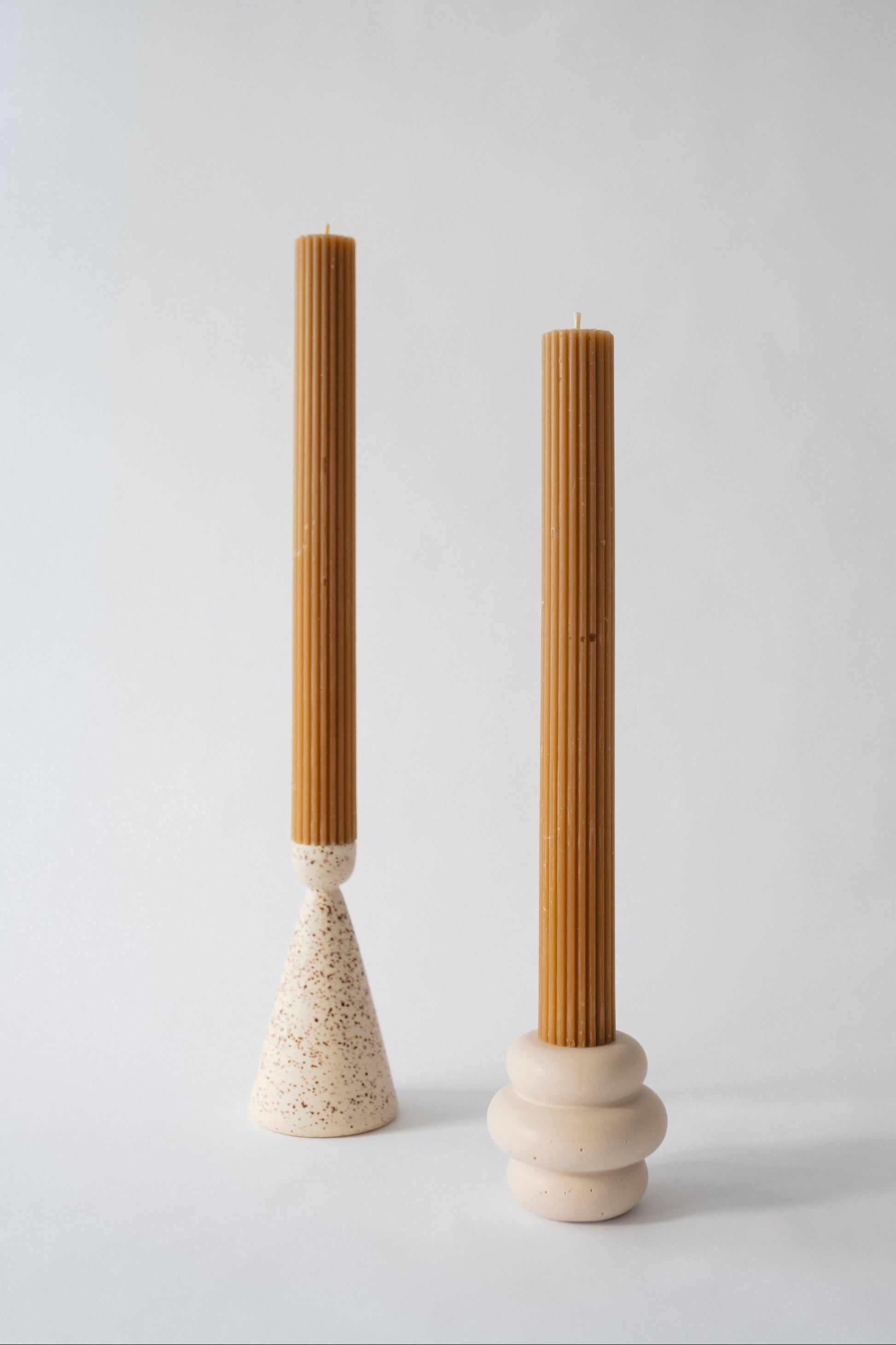 Two tall, cylindrical taper candles with a grooved texture, one with a beige base and the other with a brownish-one, set against a neutral background.