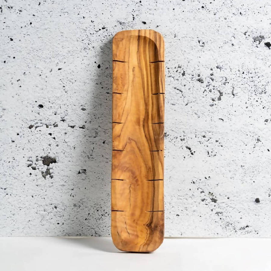 A rectangular olive wood serving tray with a carved recessed slot down the center and engraved linear markings, shown on a plain white background.