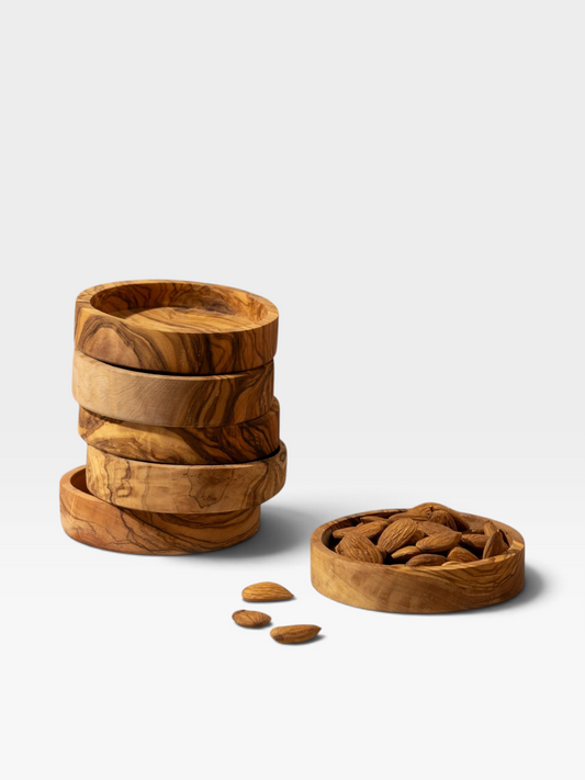 Four round, shallow wooden bowls with a natural olive wood grain pattern, with three stacked, one open and filled with almonds, on a light gray background.