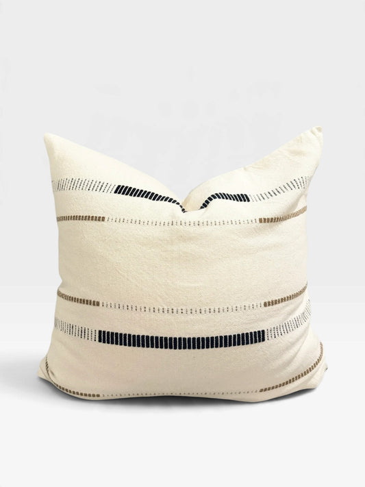 A large square throw pillow with an ivory fabric and dotted woven lines in black and soft brown photographed against a soft white background.