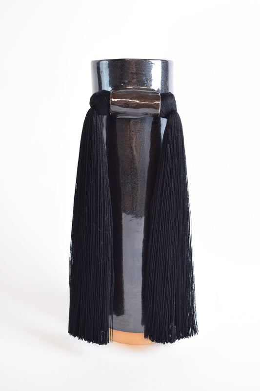 A black stoneware vase with smooth cotton fringe hanging from the rim, displayed against a white background.