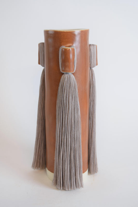 A terracotta colored stoneware vase with grey fringe detail, displayed against a neutral background.